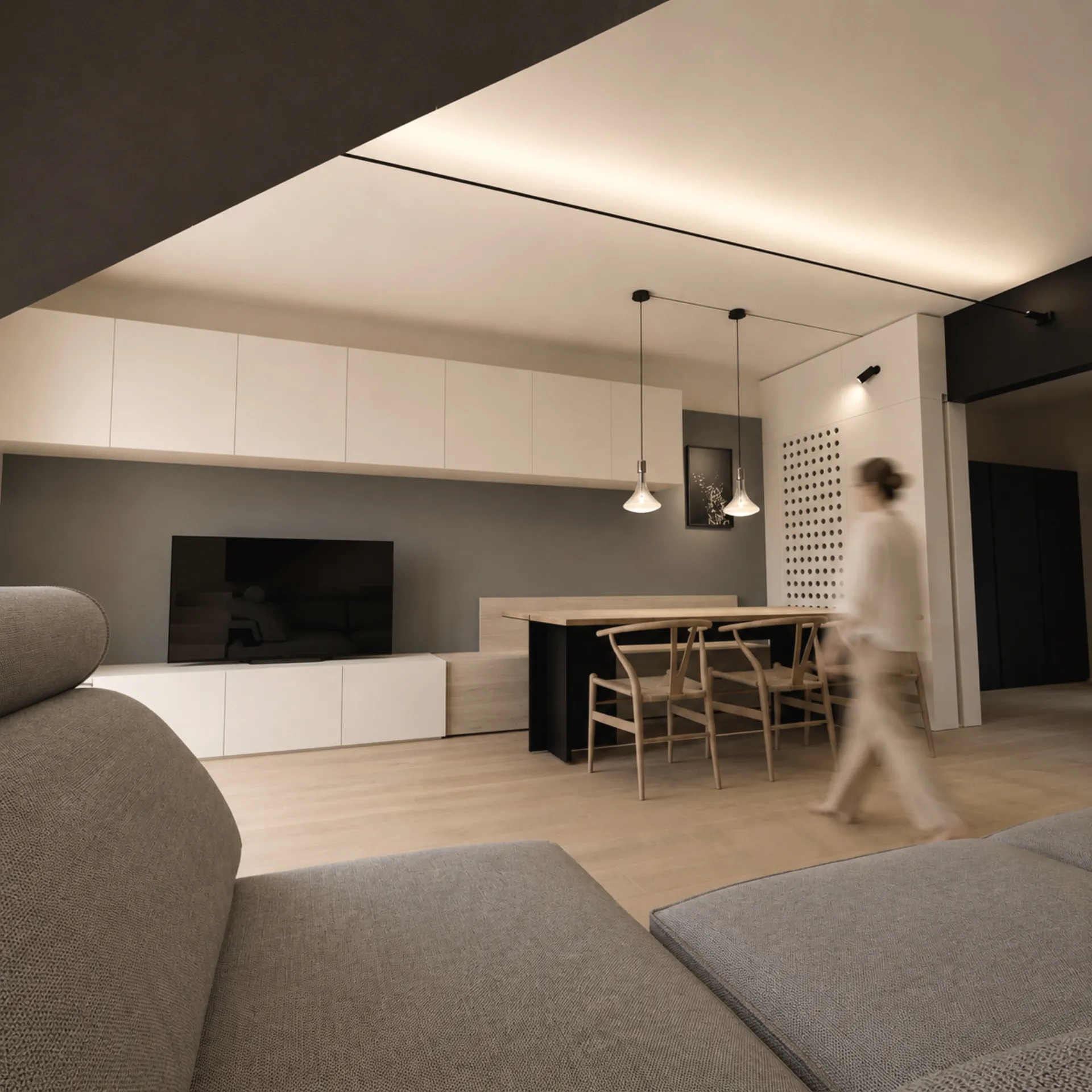 Il soggiorno di Villa M: una lama di luce attraversa il soffitto, una figura cammina sfocata verso la zona pranzo